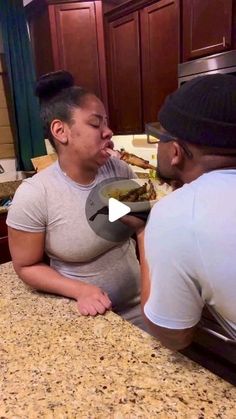 a man and woman sitting at a kitchen counter with food in front of their faces