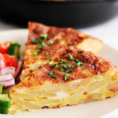 a white plate topped with a slice of quiche next to a bowl of salad