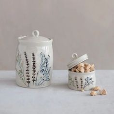 two ceramic containers with flowers on them sitting next to each other, one is filled with nuts