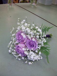 a bouquet of purple roses and white baby's breath flowers on a table top