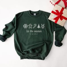 a green sweatshirt with the words tis the season to be jolly on it next to a present box