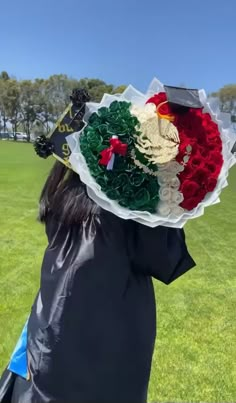 a woman wearing a black graduation gown holding a bouquet of flowers in front of her head