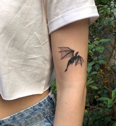 a woman's arm with a small black bat tattoo on the left inner arm