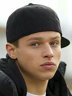 a young man wearing a black hat and jacket looking off to the side with his eyes wide open