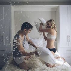 two women sitting on top of a bed covered in fluffy white sheets