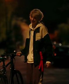 an older woman is standing next to her bike on the side of the road at night