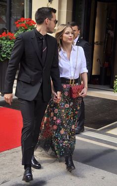 a man and woman are walking down the street in front of a building with red flowers