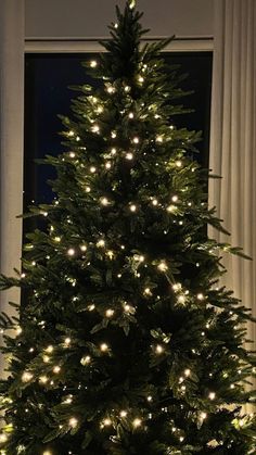 a lit christmas tree in front of a window