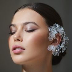 a woman with flowers in her hair is wearing large ear clips and has eyes closed