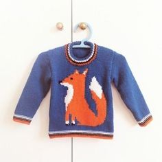 a blue sweater with an orange fox on it hanging from a hook in front of a white wall