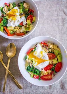 two white bowls filled with food next to gold spoons on top of a table