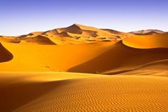 sand dunes with mountains in the background under a blue sky filled with wispy clouds