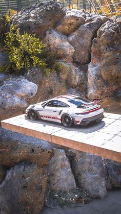 a white sports car is parked on a platform in front of some rocks and trees