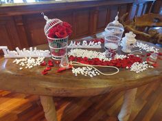 a wooden table topped with lots of red roses and birdcages on top of it