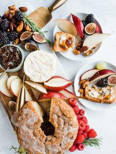 an assortment of fruit and cheeses on a cutting board next to plates with spoons