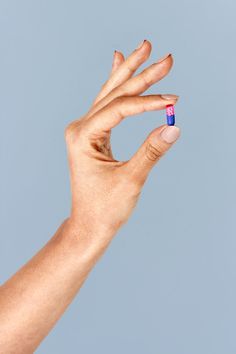 a person's hand holding a small blue and pink pill in their left hand