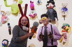 two people standing next to each other holding microphones in front of stuffed animals on the wall