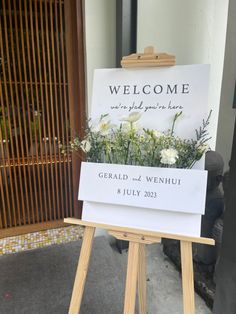 a welcome sign sitting on top of a wooden easel next to a building door