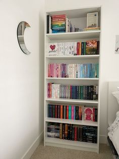 a bookshelf filled with lots of books next to a white wall and bed