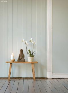 a buddha statue sitting on top of a wooden table next to a vase with flowers