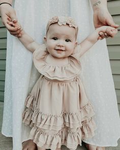 a woman holding the hand of a baby girl in her arms while wearing a dress