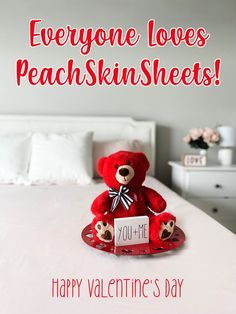 a red teddy bear sitting on top of a bed next to a sign that says everyone loves peachskinsheets