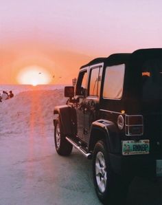 a jeep parked on the beach at sunset with people swimming in the water behind it