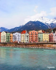 colorful buildings line the shore of a body of water in front of snow capped mountains