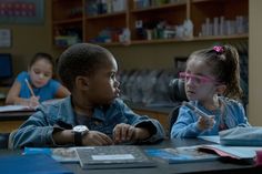 two children are sitting at a table with books and pens in front of their faces