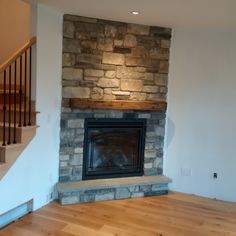 an empty living room with a stone fireplace and wood flooring, along with stairs