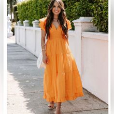 a woman in an orange dress is standing on the sidewalk with her hands in her pockets