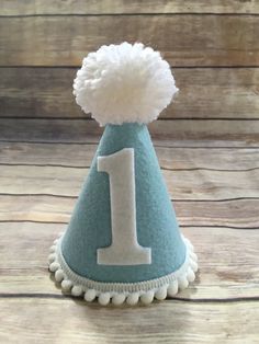 Please read shop announcement for current processing times and updates. Your birthday boy will look absolutely adorable in this mini birthday hat for his half birthday or whole birthday! Perfect for a party or photo shoot. The hat is available in 2 sizes, Mini which is 5 inches tall and 4 inches wide or Full size which is 7 inches tall by 5 inches wide. It features baby blue felt with a white number of your choice. White mini pom pom ribbon is attached along the base of the hat with a yarn Pom P Fun White Birthday Party Supplies, Cute White Hat For First Birthday, Playful White Party Supplies For First Birthday, White Fun Party Supplies For Birthday, Fun White Party Supplies For Birthday, Playful Blue Hat As A Gift, Playful Blue Hat As Gift, Playful Blue Hat For Gift, Playful Blue Hats For Gifts