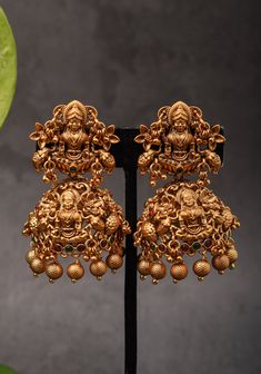 Jhumka - a gorgeous piece of jewelry named for the way it dangles playfully! One is sure to fall in love with these earrings. If you ask why, we will say it's simply because they are sure to add beauty to one's face and overall look. Comes in the classic jhumka shape pattern with lakshmi seated in padmasan pose on a Lotus pattern in an antique dark gold finish. Note: This jewelry has no precious metals or stones.  Note: Some of the pics are close up shots to show detail and may make the product appear larger. Please refer to the measurements picture for better perspective on size. Lotus Pattern, Jhumka Earrings, Dark Gold, Shape Pattern, Shape Patterns, Wedding Outfit, Precious Metals, Gold Finish, Favorite Jewelry