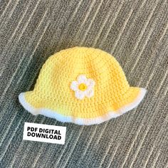 a yellow crocheted hat with a flower on it sitting on the floor next to a gray carpet