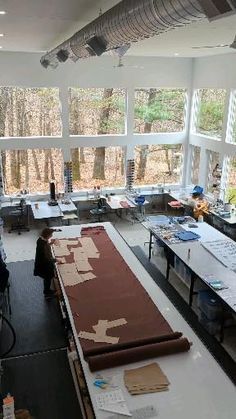 a large room filled with lots of tables and chairs in front of big windows that look out onto the woods