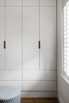 a bedroom with white cupboards and wooden flooring, along with a round ottoman in the foreground