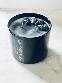 a black candle with skulls on it sitting on a marble counter top next to a white wall