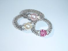 three bracelets with pearls and beads on a white surface, one has a pink bead around the clasp