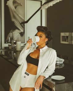 a woman drinking from a cup while standing next to a counter