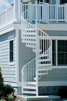 there is a white spiral staircase in front of a gray and white house on the beach