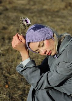 a woman sitting on the ground with a flower in her hand and wearing a purple hat