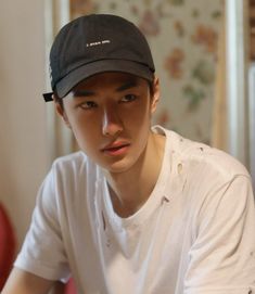 a young man wearing a black hat sitting in front of a red chair and looking at the camera