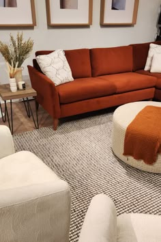 a living room with two couches and a round ottoman on the floor in front of three framed pictures