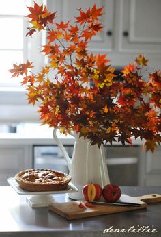 an apple pie sitting on top of a table next to a vase filled with leaves