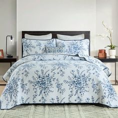 a blue and white comforter set with flowers on it in the middle of a room