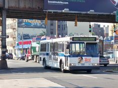 a city bus driving down the street under a large overpass with buildings in the background