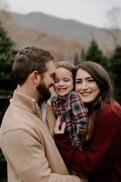 a man, woman and child are smiling at the camera in front of some trees