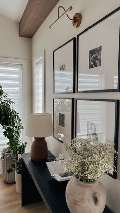 a vase with flowers sitting on a table next to a lamp and pictures hanging on the wall