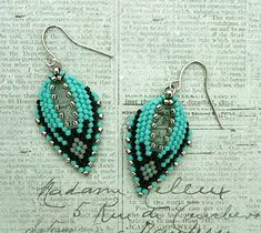 the beaded earrings are made with turquoise beads and silver metal findings on top of an old newspaper page