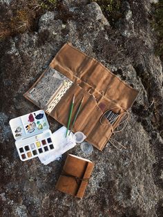 an artist's kit sits on the ground next to some rocks and paintbrushes